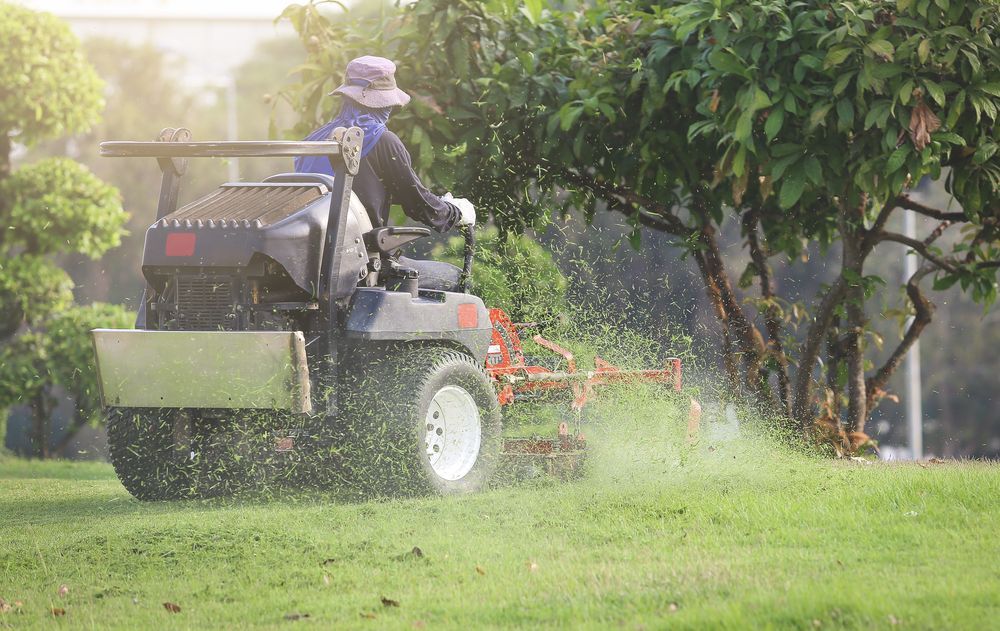 A Person Wearing a Hat Operates a Riding Lawn Mower — Old Mates Grass Cutters in Deeragun, QLD