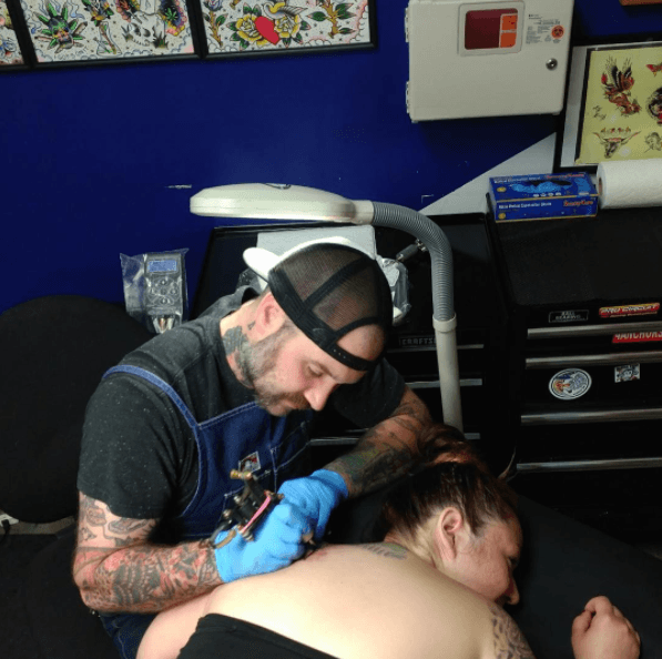 A man is getting a tattoo on a woman 's back