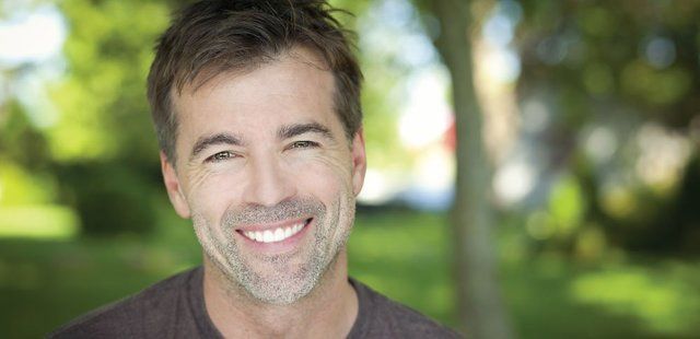 A man with a beard is smiling for the camera in a park.