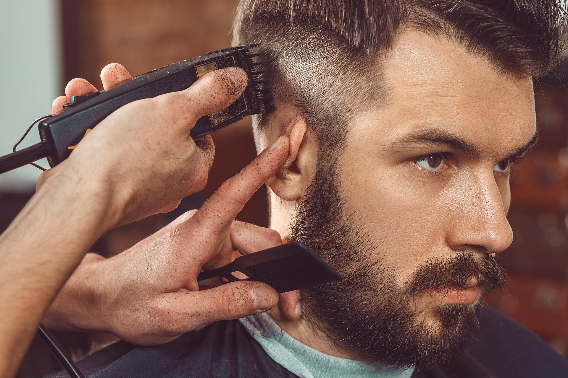 A man with a beard is getting his hair cut by a barber.