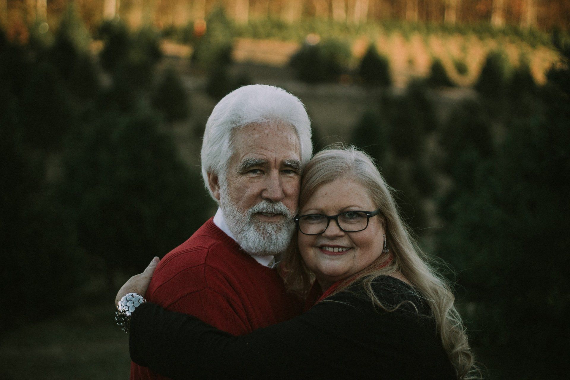 A man and a woman are hugging each other in front of a christmas tree farm.