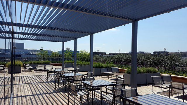 A patio with tables and chairs under a pergola on a sunny day.