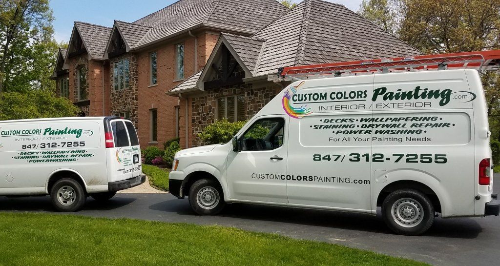 Two white vans are parked in front of a large house.