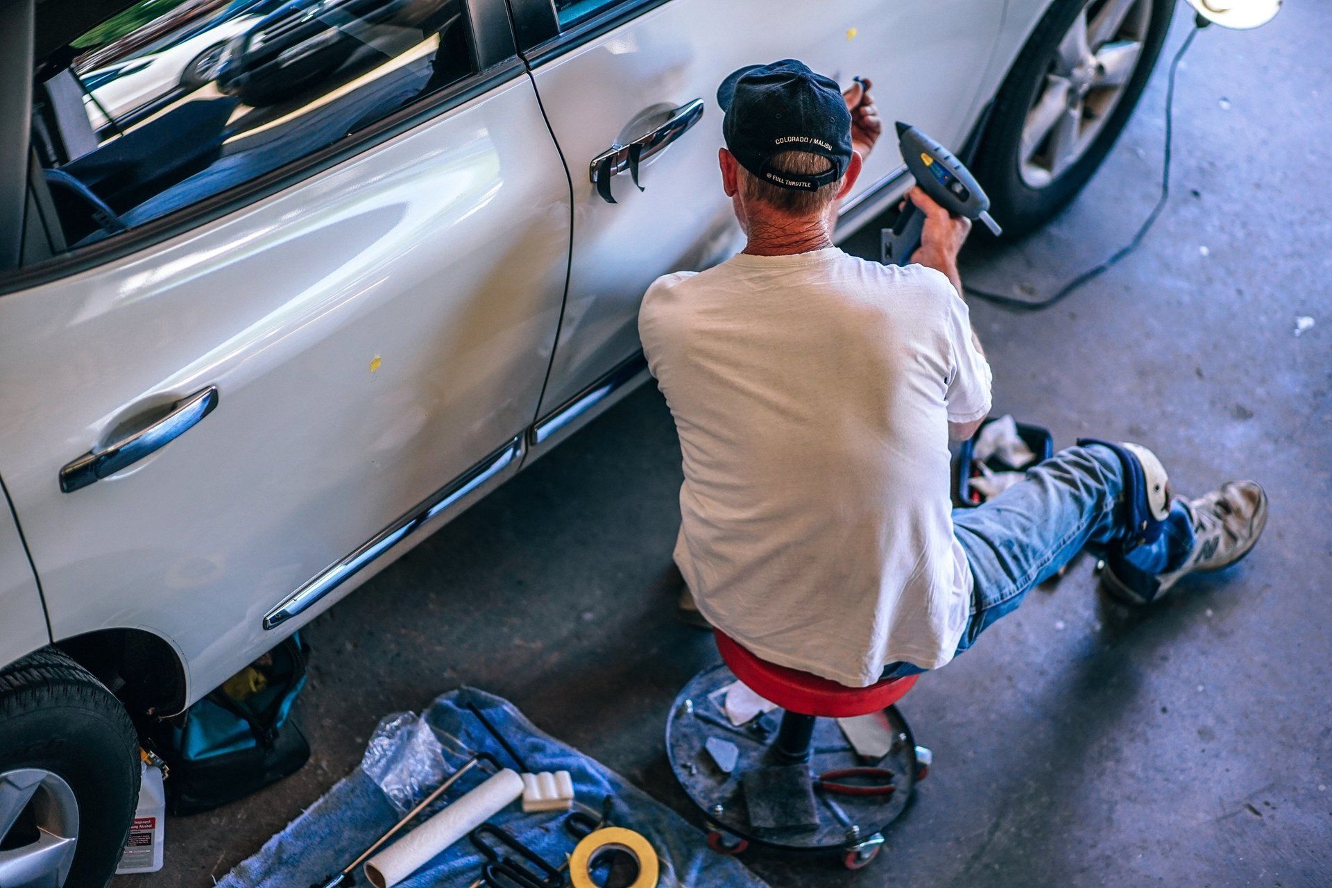 A man is sitting on a stool working on a car in a garage.