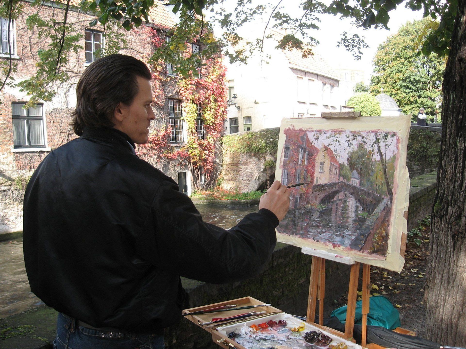 A man in a black jacket is painting on an easel