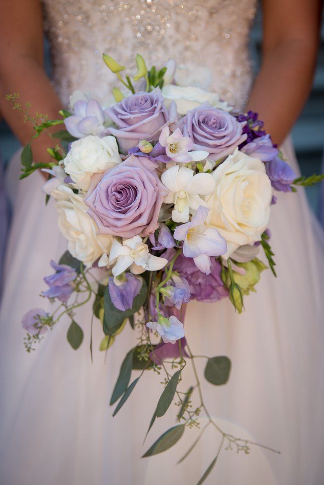 A bride in a white dress is holding a bouquet of purple and white flowers.