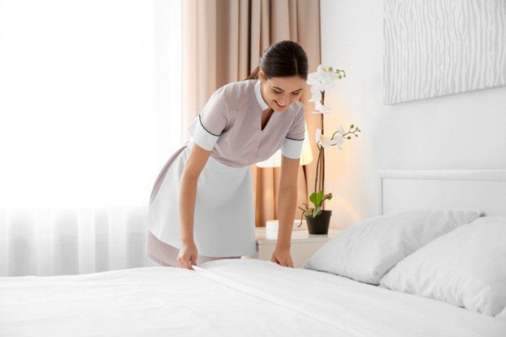 A maid is making a bed in a hotel room.
