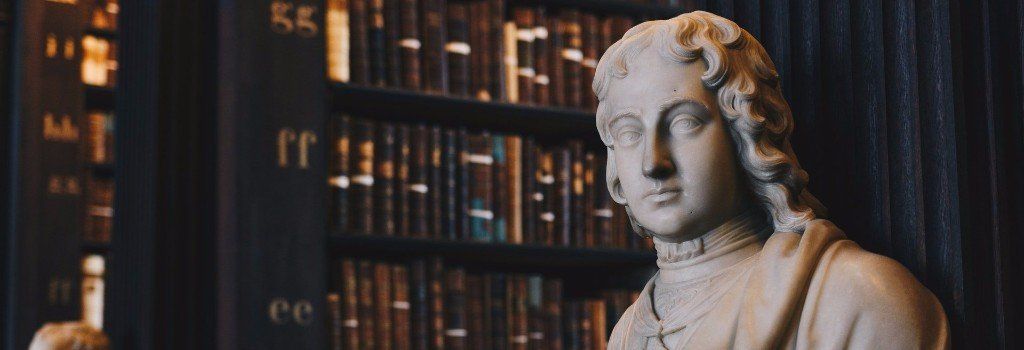 A statue of jesus is sitting in front of a bookshelf in a library.