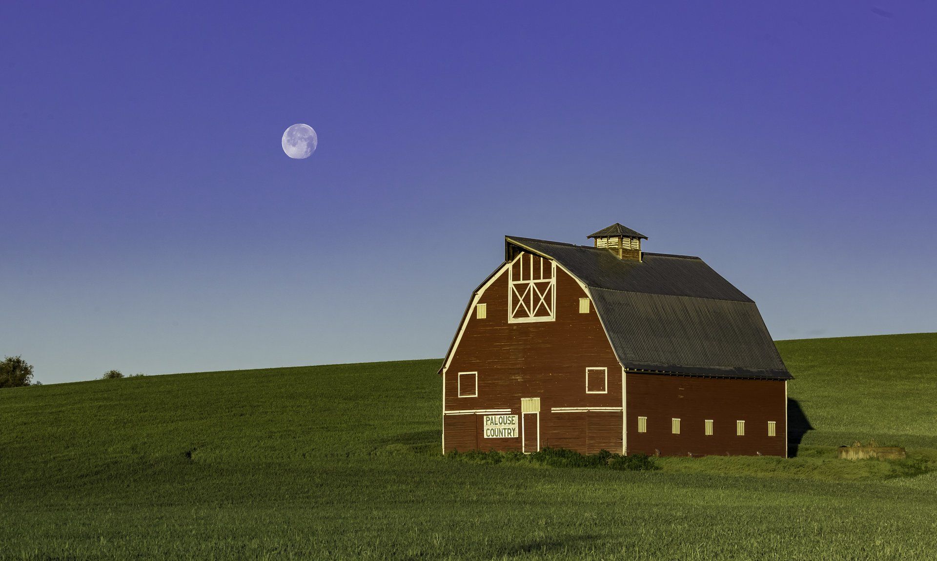 A red barn in a field with a full moon in the background