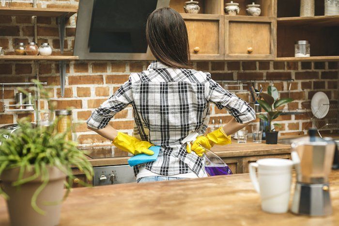 A woman wearing yellow gloves is cleaning a kitchen counter.