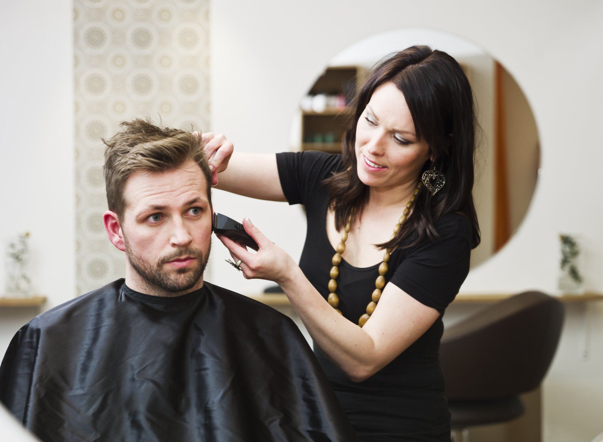 A woman is cutting a man 's hair in a salon.