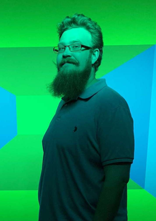 A man with a beard and glasses is standing in front of a green and blue background.