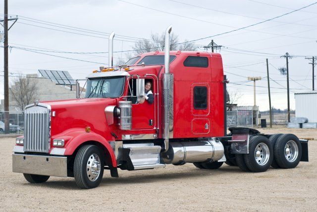 A red semi truck is parked in a dirt field