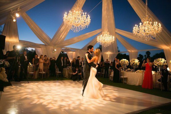 A bride and groom are dancing under a tent at their wedding reception