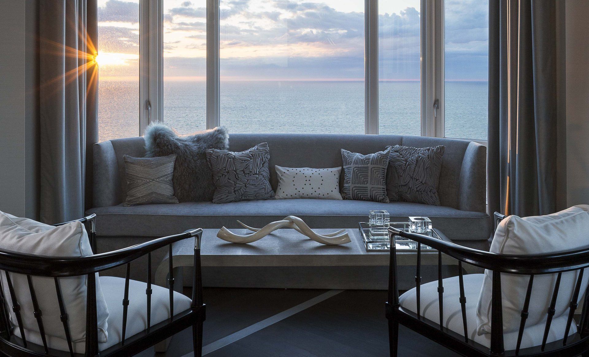 A living room with a couch , chairs and a table with a view of the ocean.