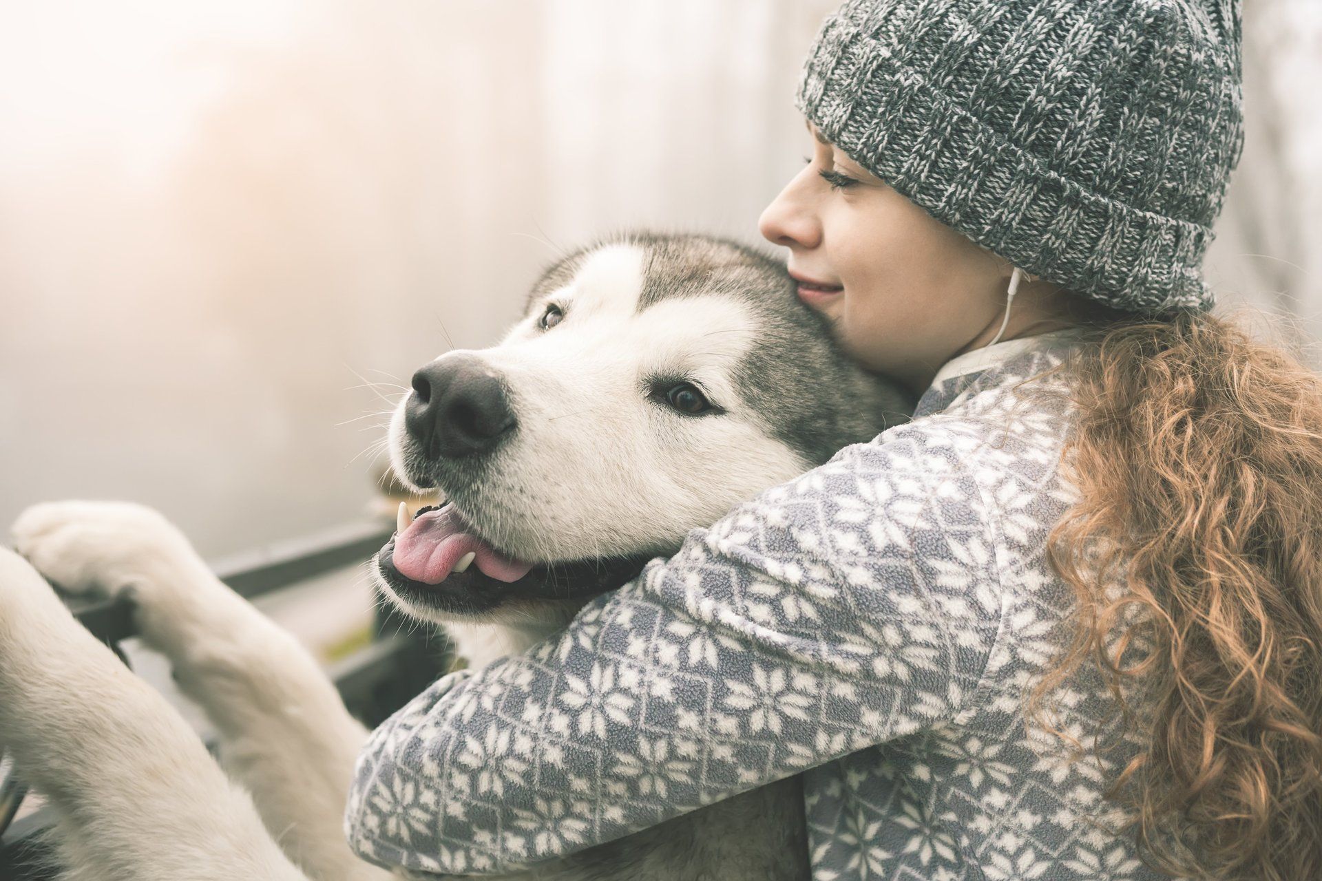 A woman in a hat is hugging a husky dog.