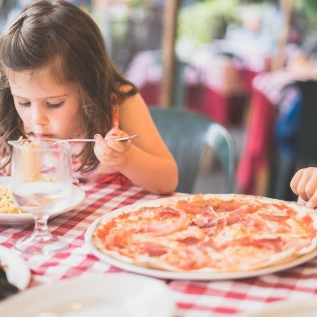 A little girl is sitting at a table eating a pizza with a fork.