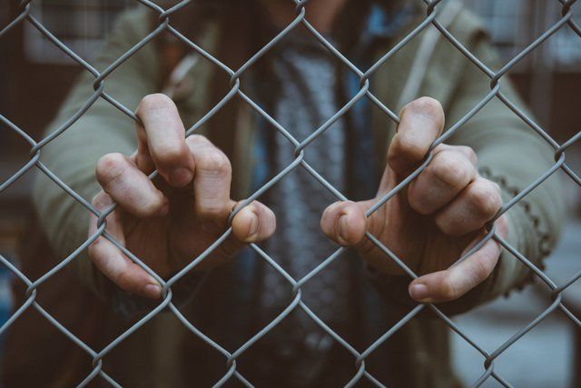 A man is holding onto a chain link fence with his hands.
