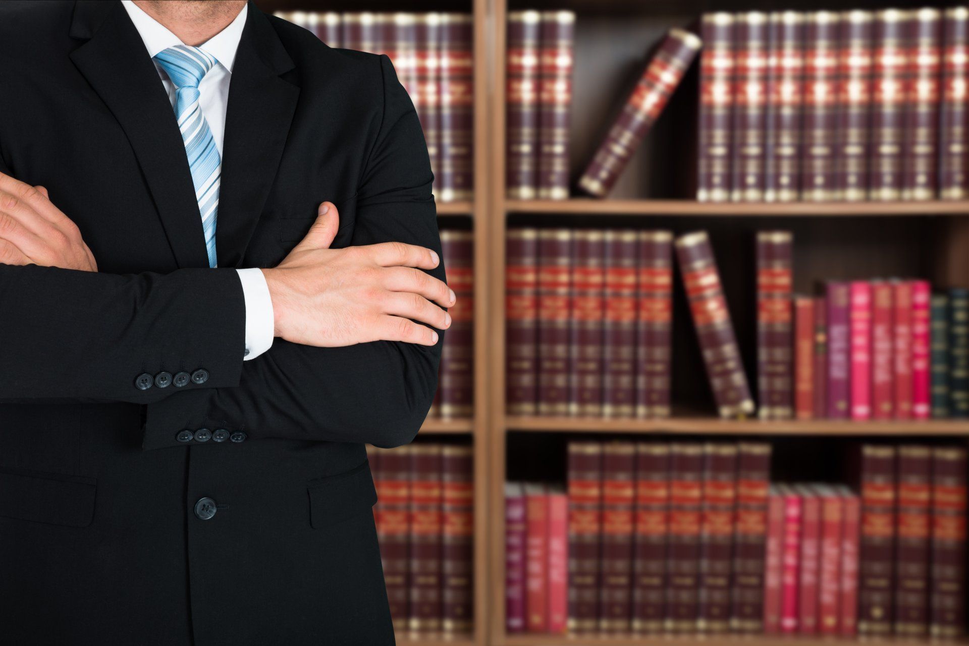 A man in a suit and tie is standing in front of a bookshelf.