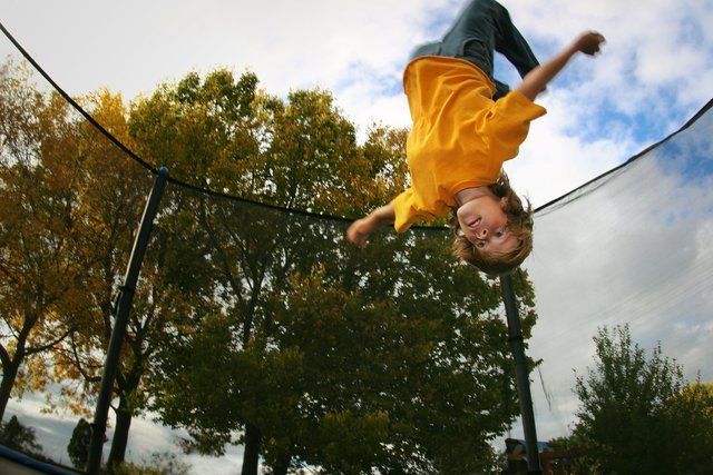 A young boy in a yellow shirt is upside down on a trampoline