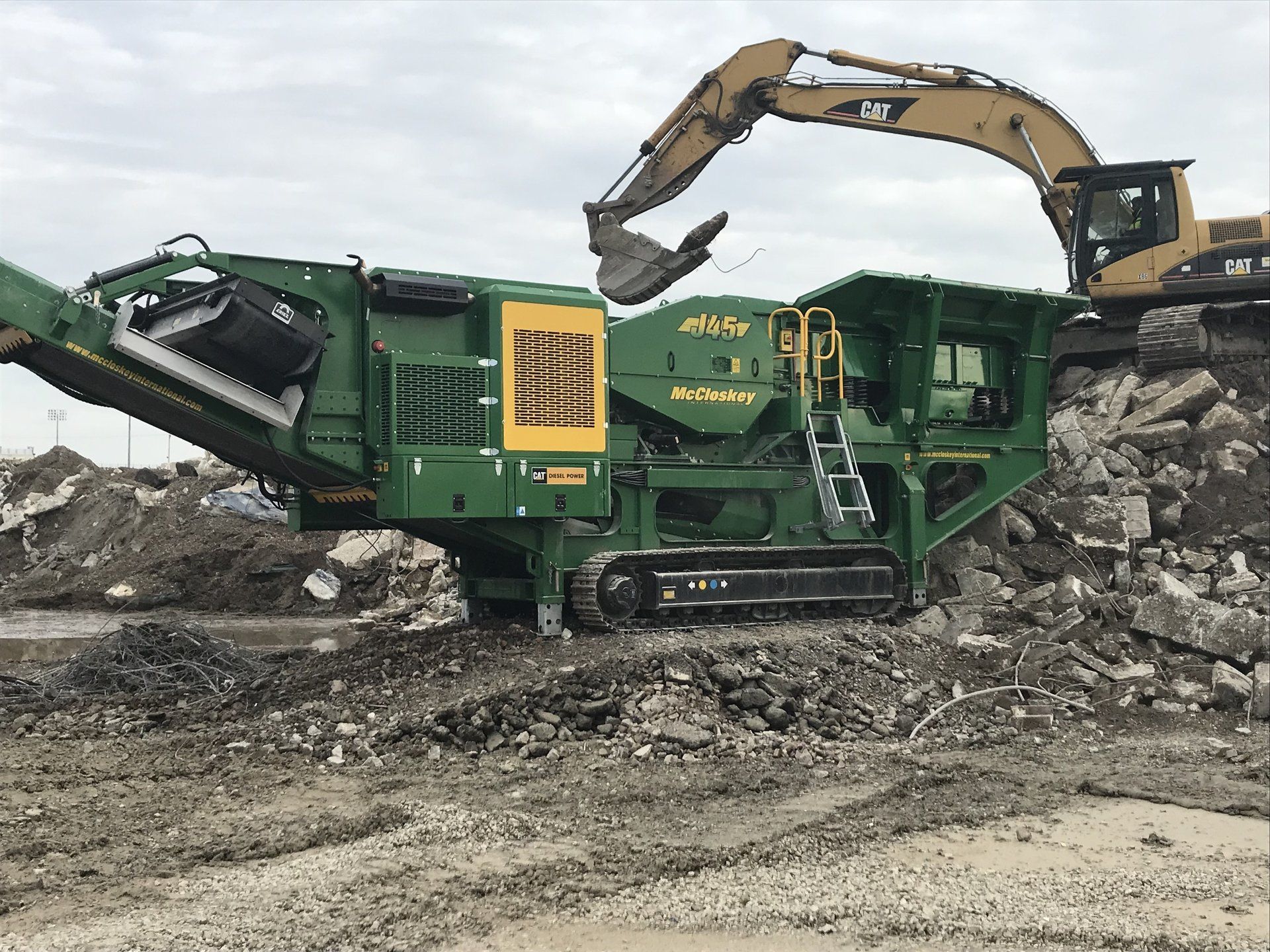 A green and yellow machine is sitting in the middle of a pile of rocks.