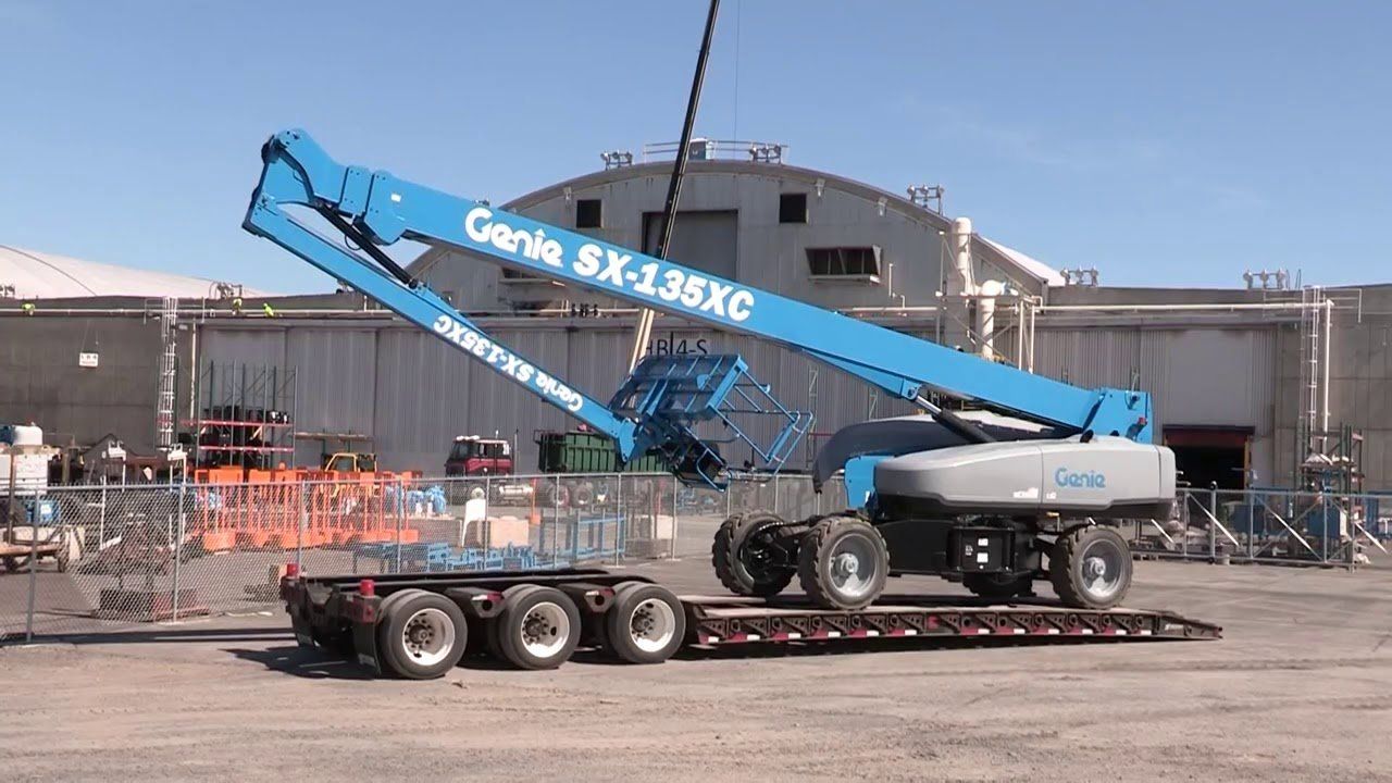 A genie lift is being lifted by a crane on a trailer.