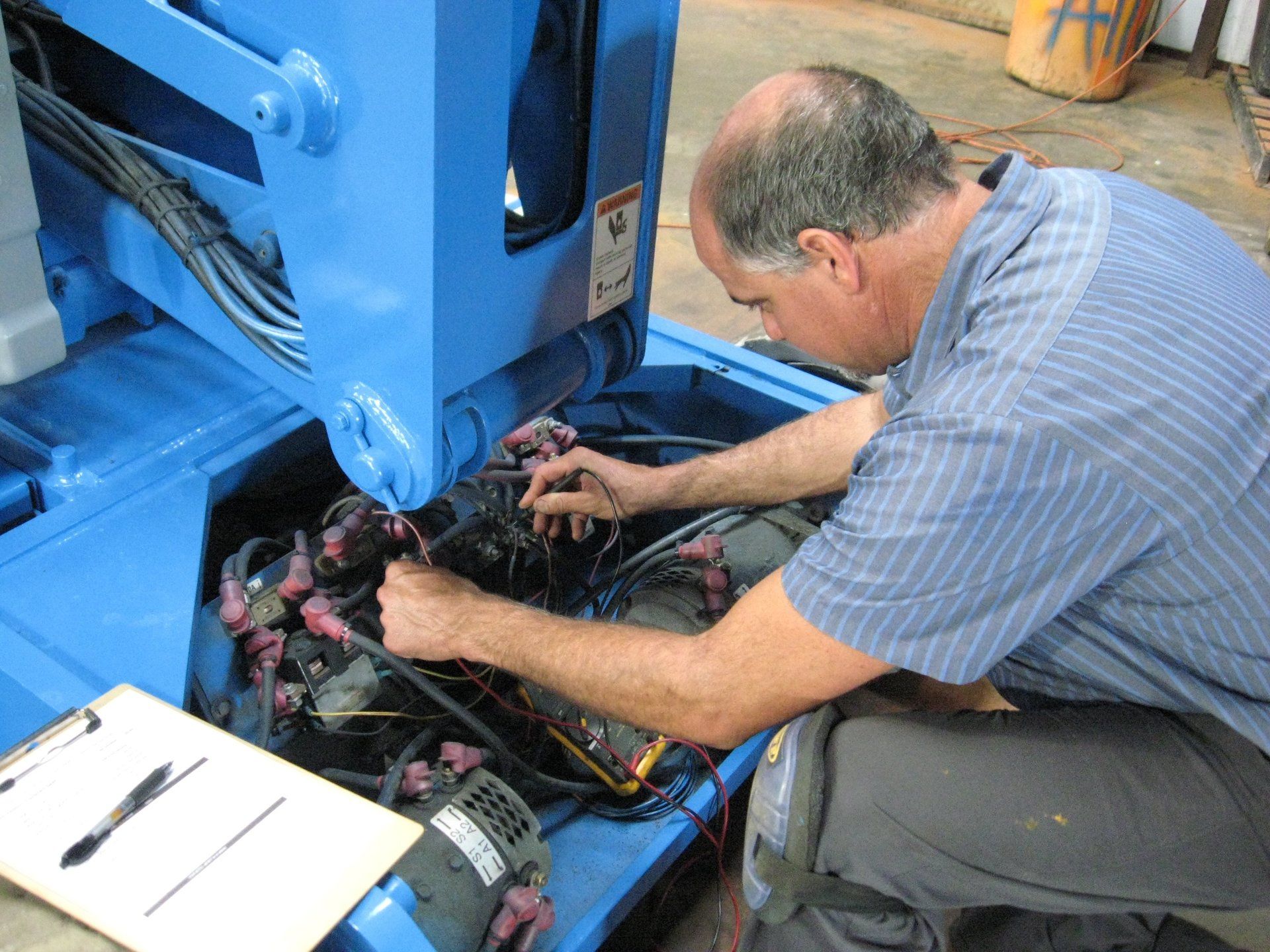 A man is kneeling down working on a blue machine