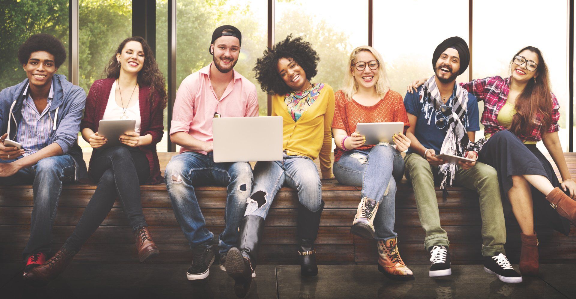 A group of people are sitting on a bench using laptops and tablets.