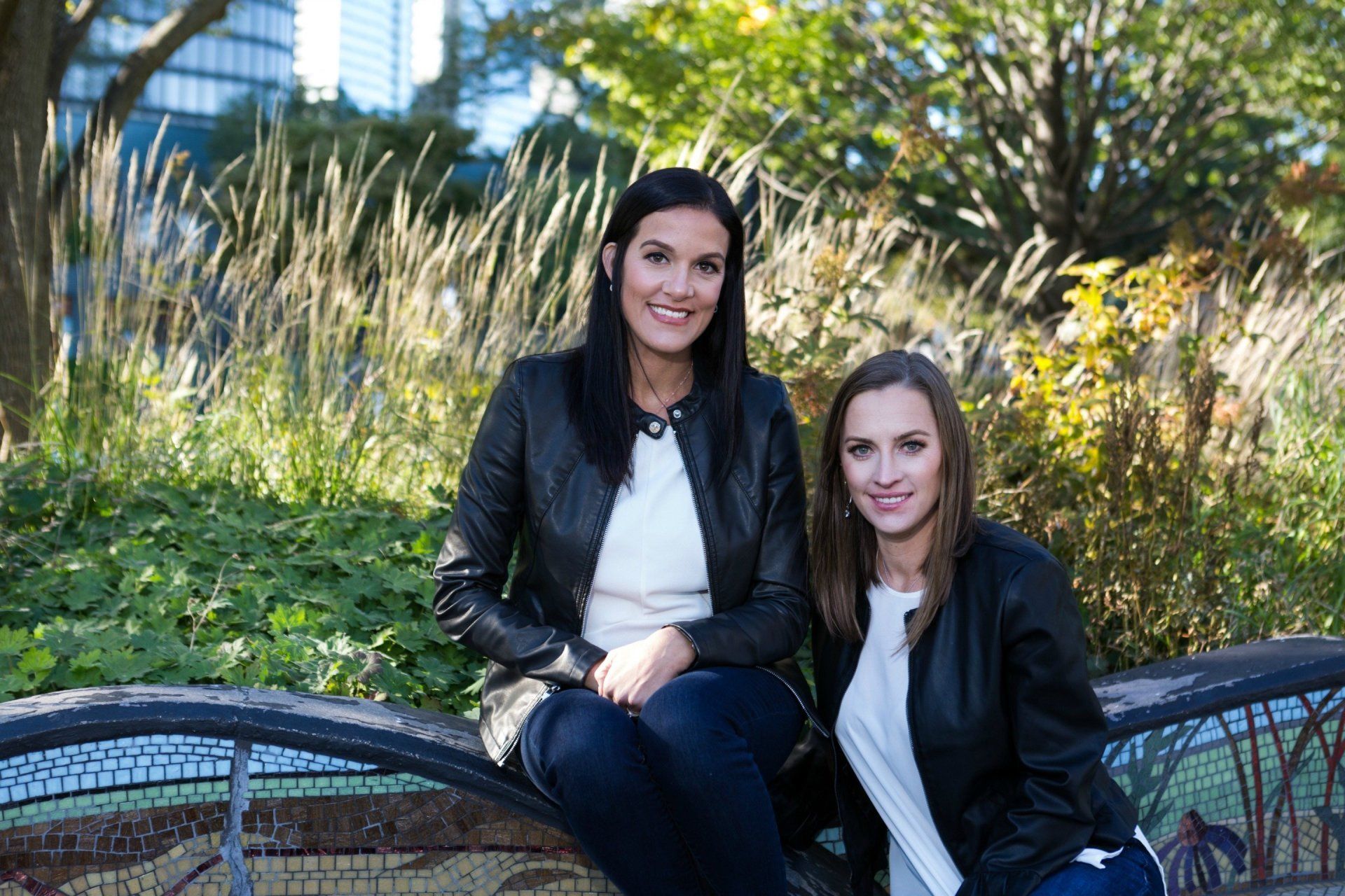 two women are sitting on a bench in a park .