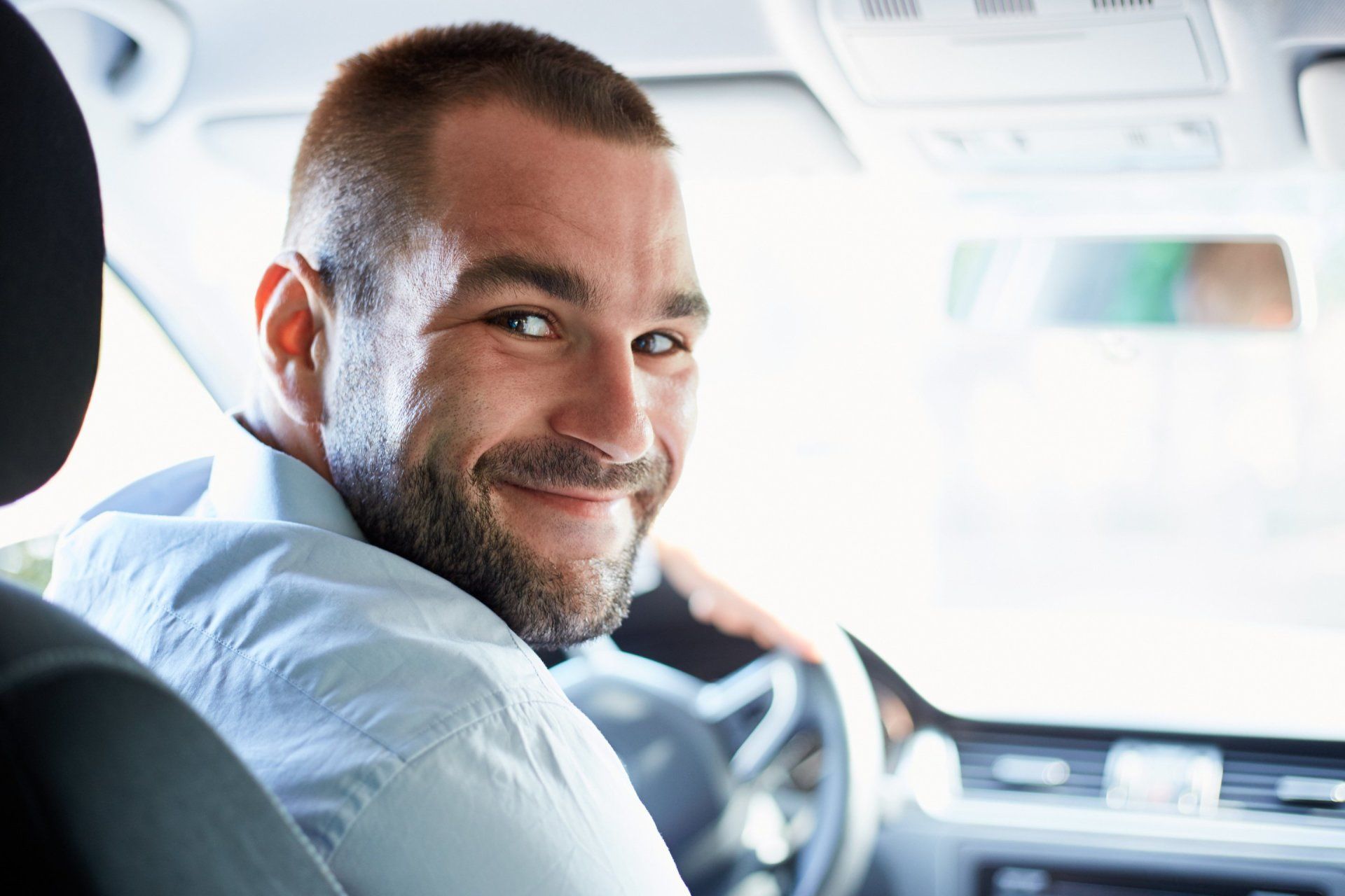 a man is sitting in the driver 's seat of a car and smiling .