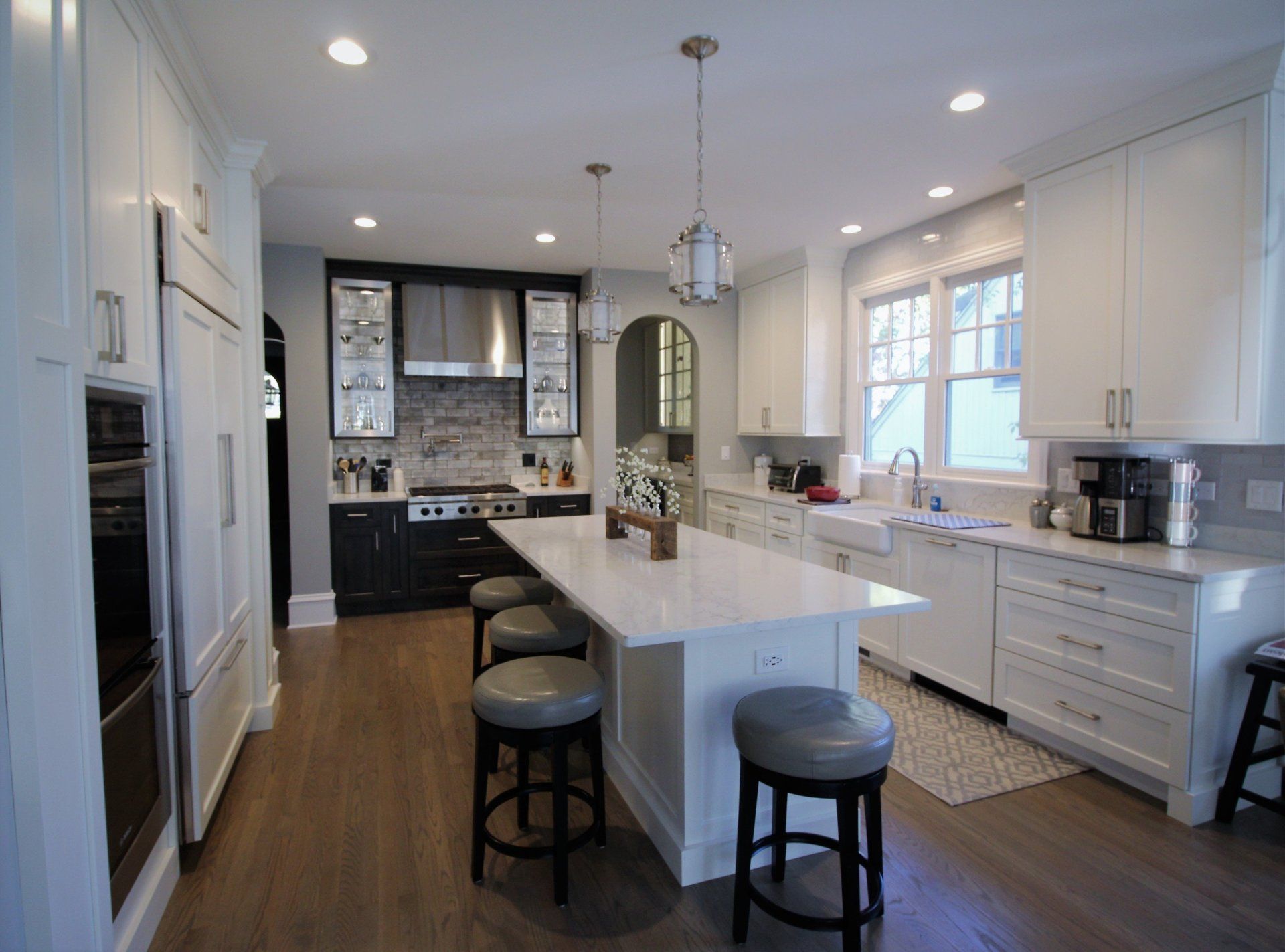 A kitchen with white cabinets and stools and a large island in the middle.