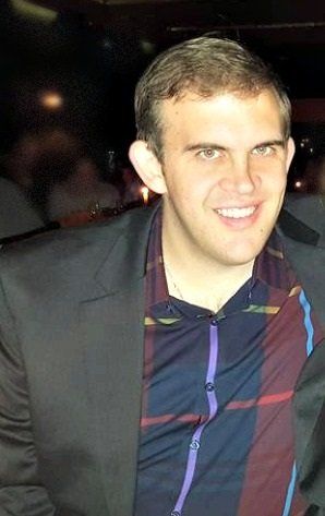 A man in a suit and plaid shirt is smiling for the camera.