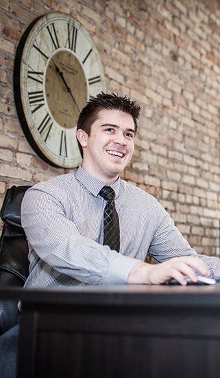 A man is sitting at a desk in front of a clock.