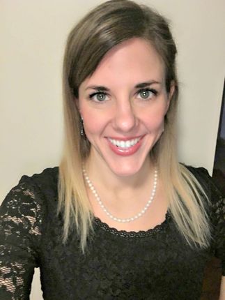 A woman wearing a black lace top and a pearl necklace smiles for the camera