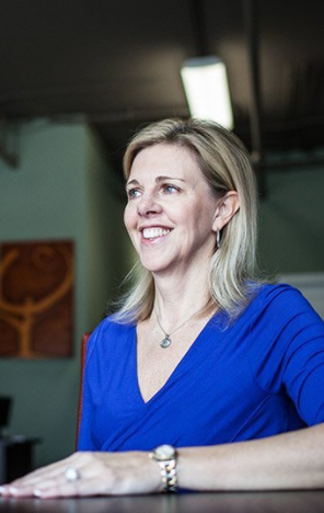 A woman in a blue shirt is sitting at a table and smiling.