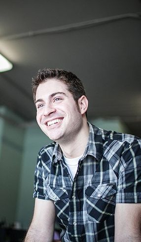 A man in a plaid shirt is smiling and looking away from the camera.