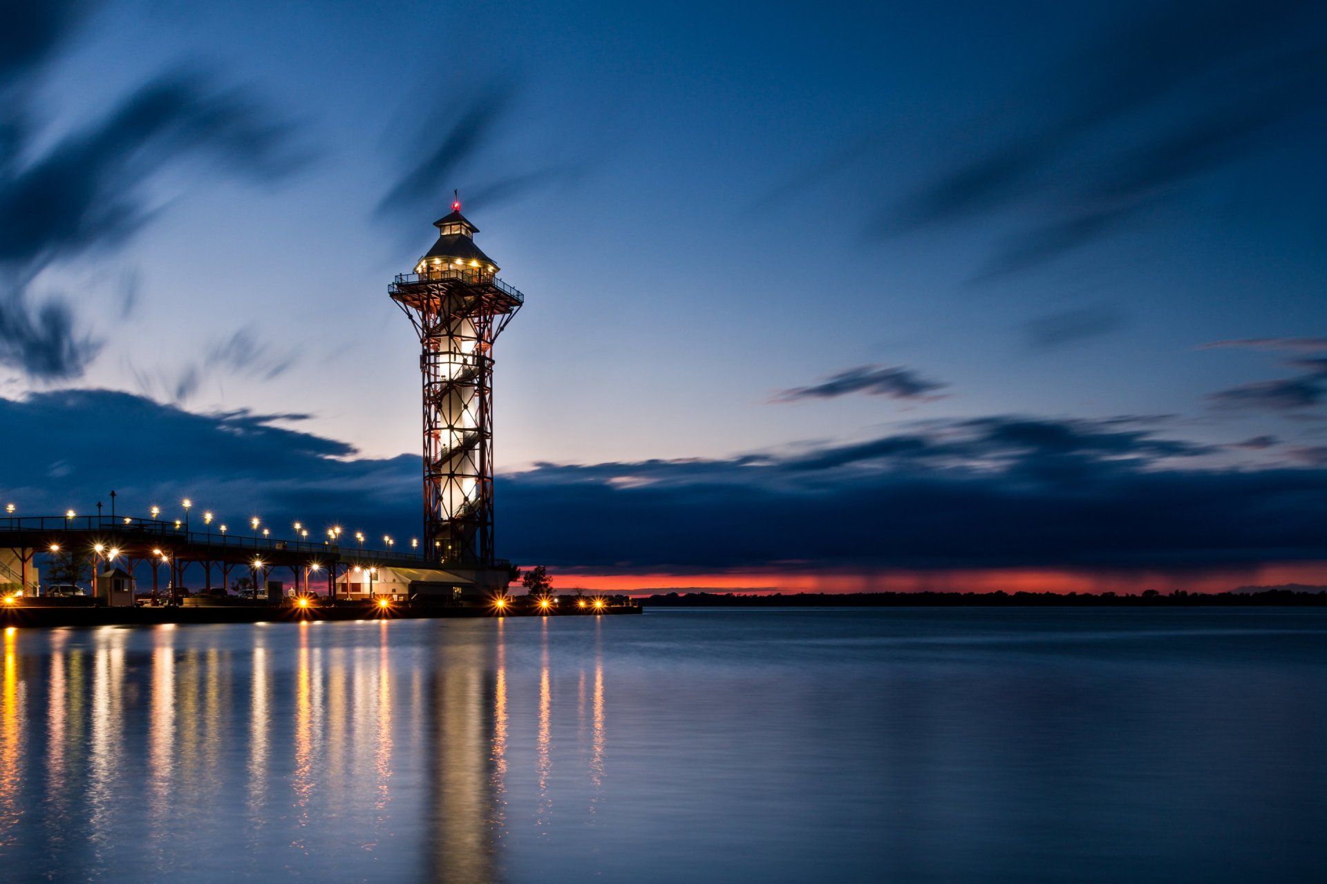 A lighthouse is lit up at night in the middle of a body of water.
