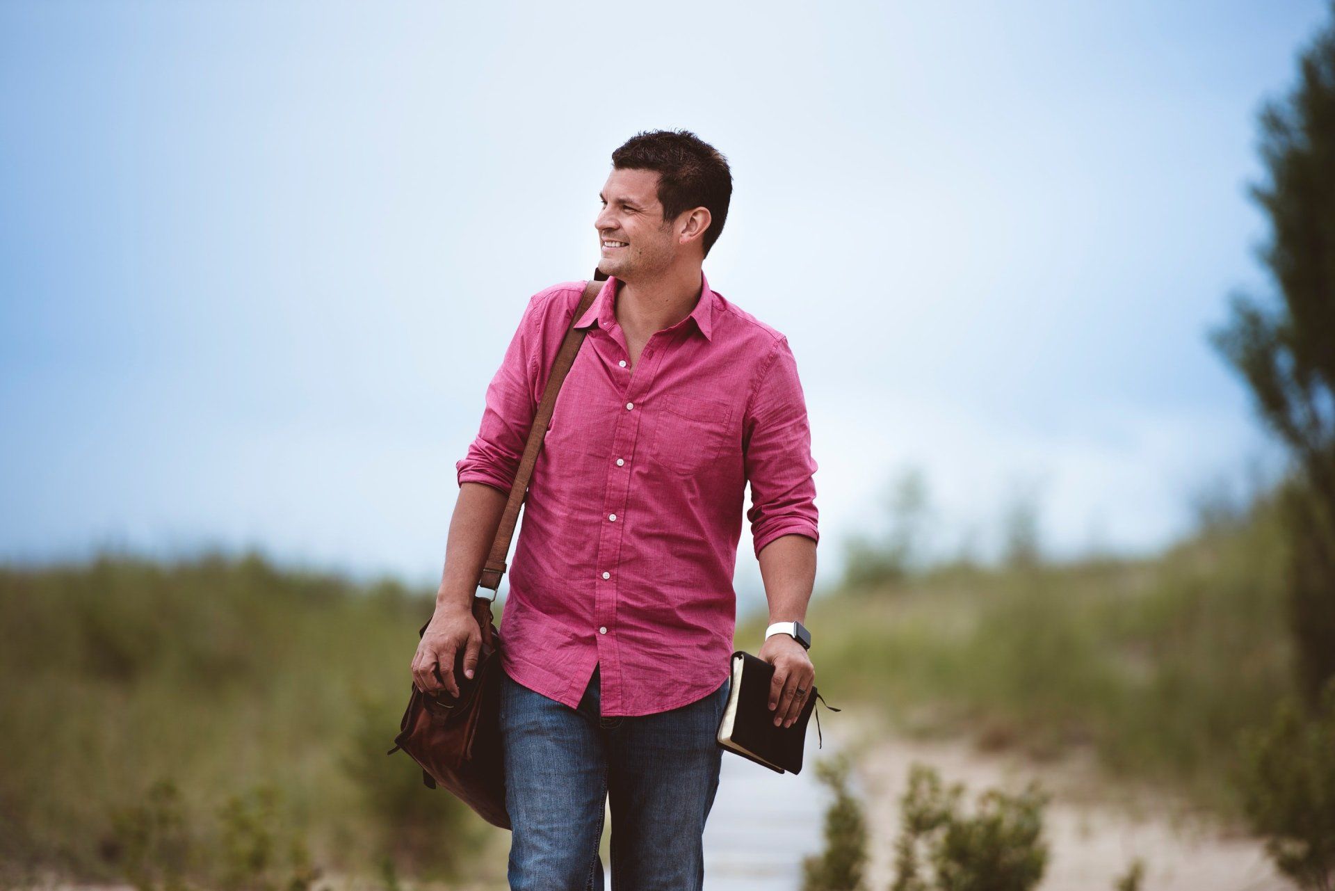 A man in a pink shirt is walking down a path holding a bible.