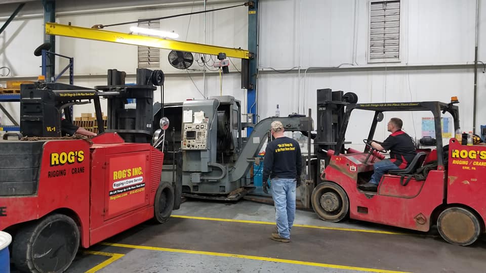 A man is standing next to a red forklift in a garage.