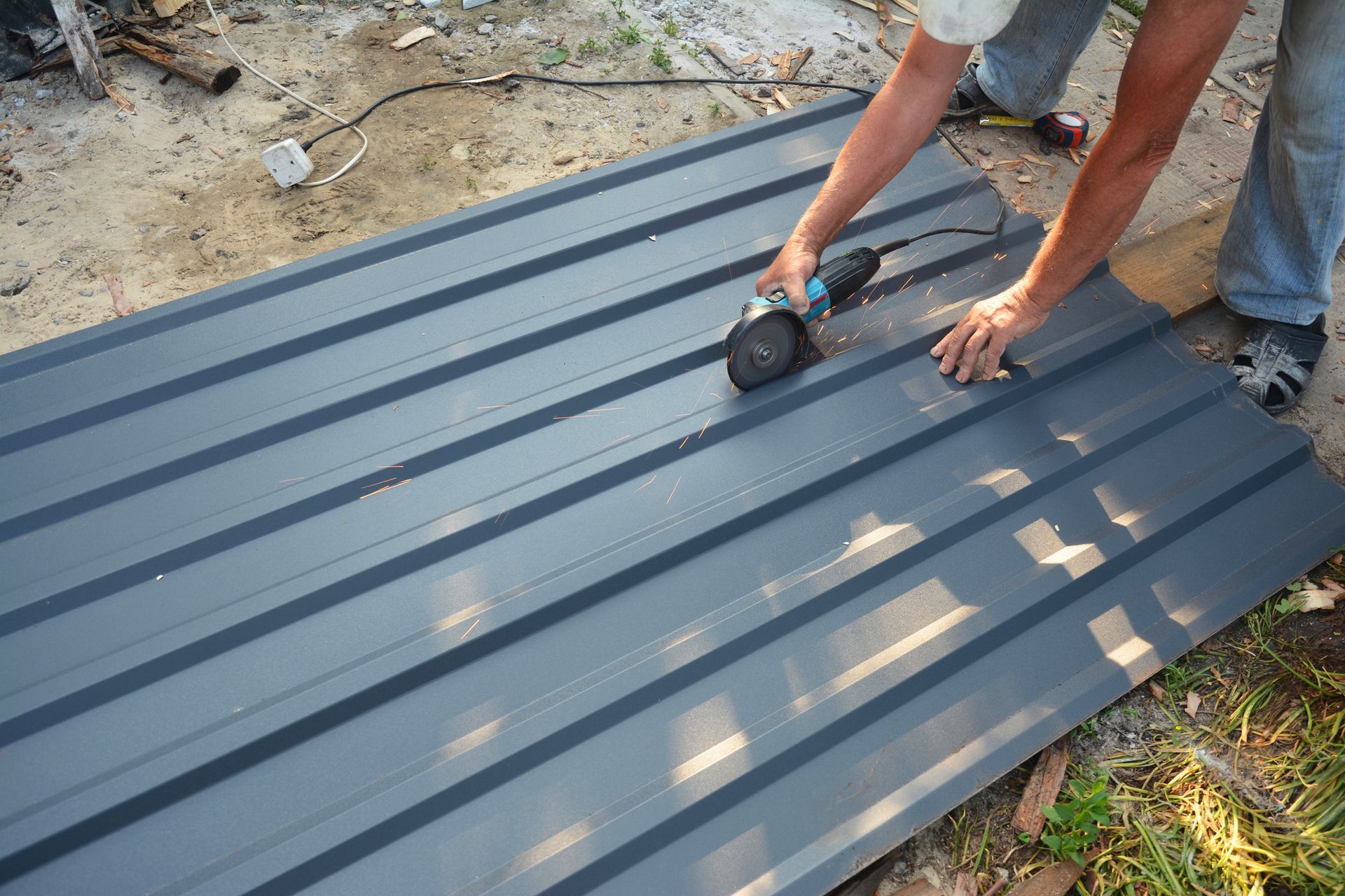 Roofer cutting metal roof sheet with a grinding machine on the ground.