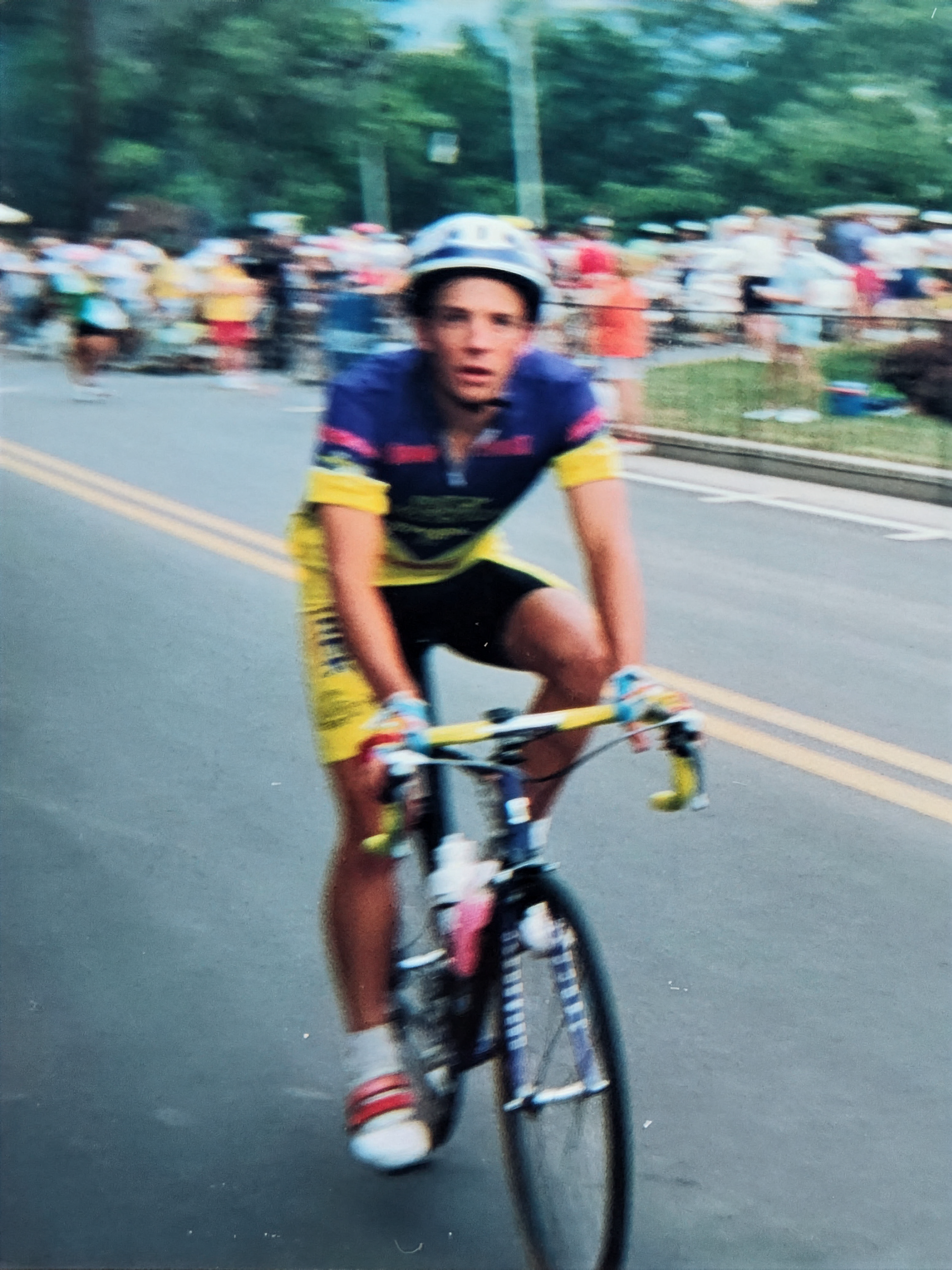 Cyclist in yellow and blue racing gear, riding a road bike on a paved road.