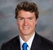 A man in a suit and blue shirt is smiling for the camera.