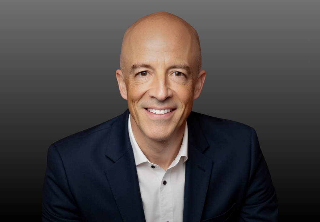 Bald man in a dark suit smiles at the camera.