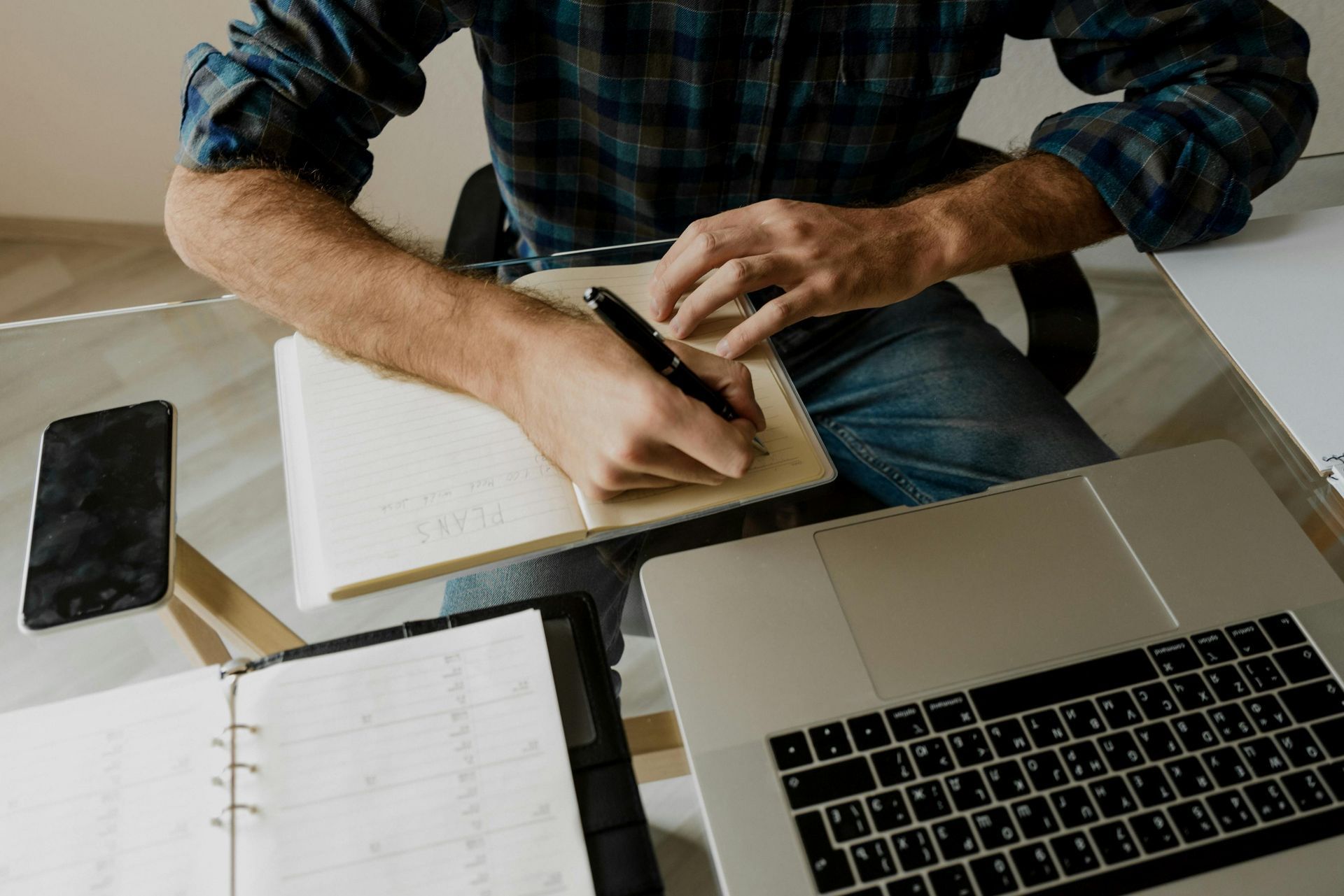 A man is sitting at a desk with a laptop and a notebook.