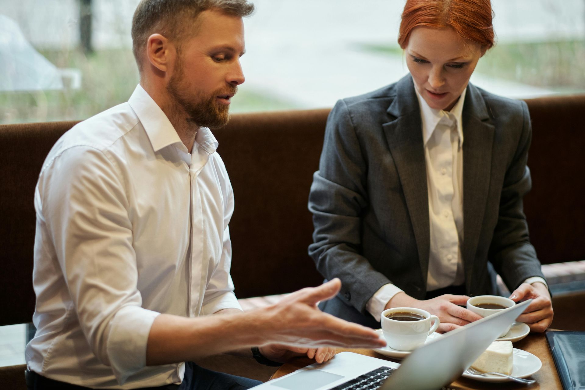 A man and a woman are sitting at a table looking at a laptop.