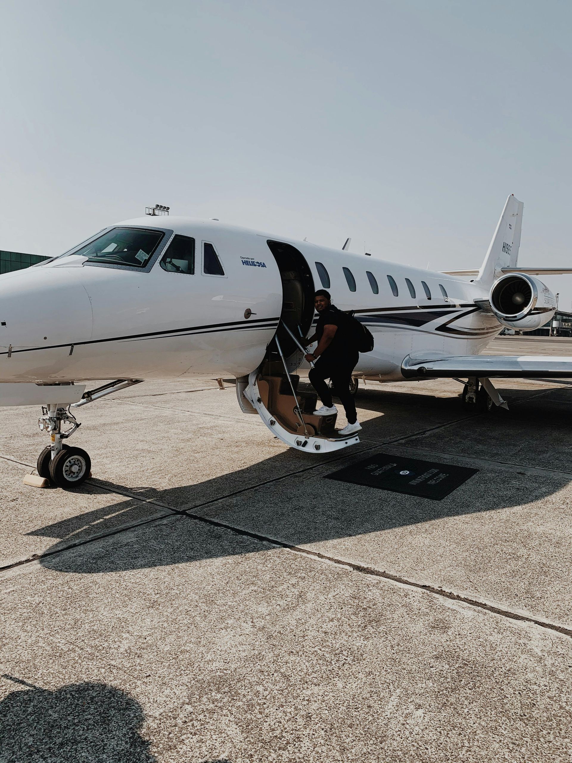 Person exiting white private jet on a tarmac on a sunny day.