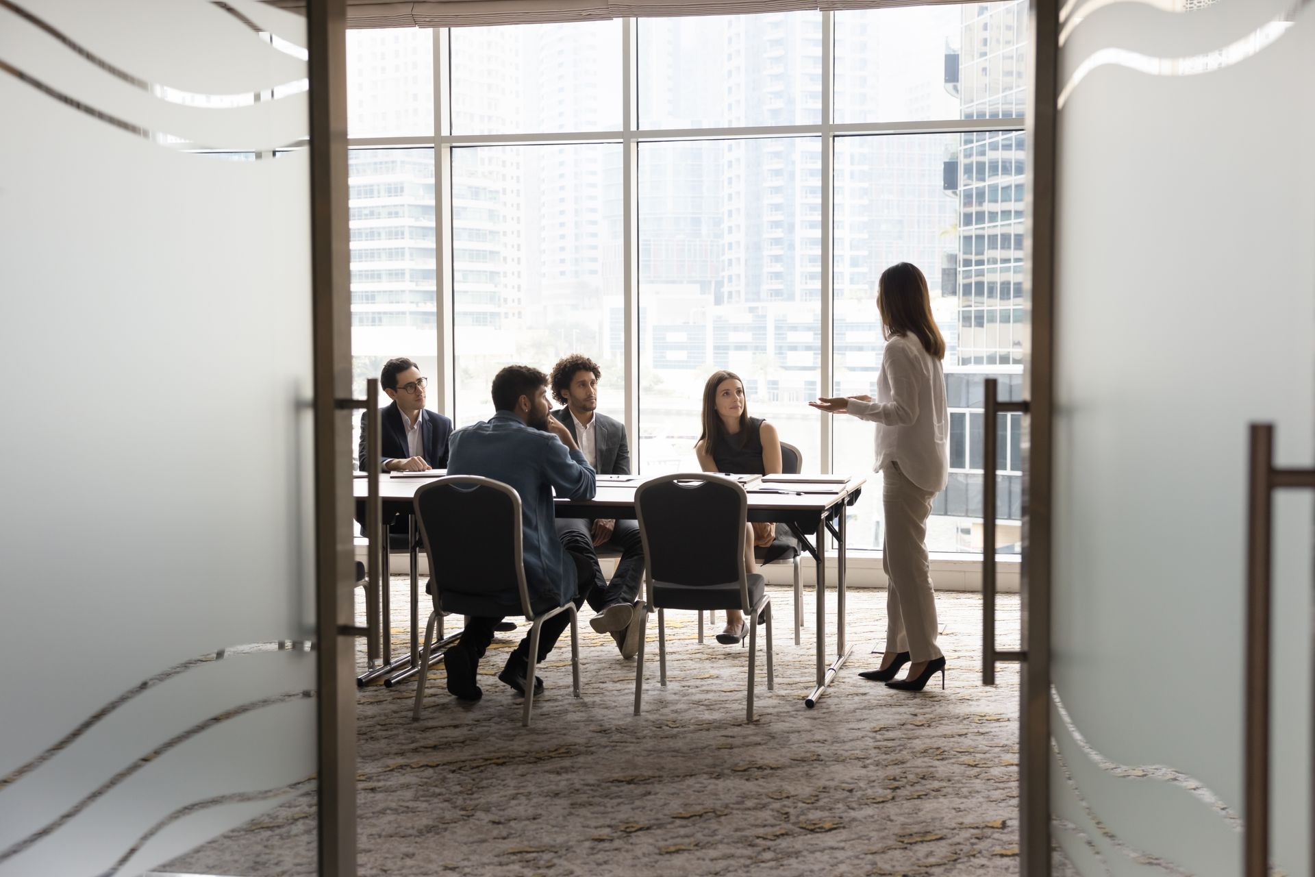 Businesswoman presenting to colleagues in a modern conference room with large windows, city view.
