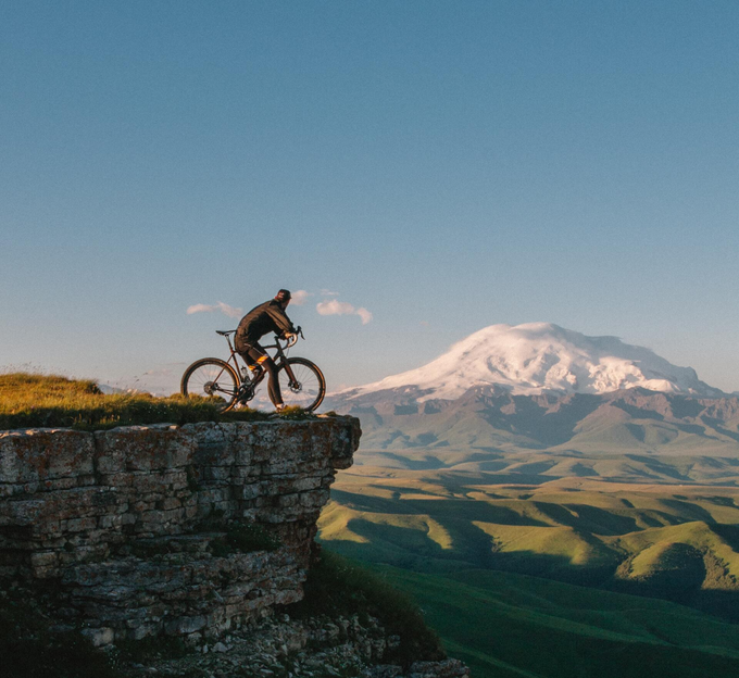 A man is riding a bike on a cliff with a mountain in the background