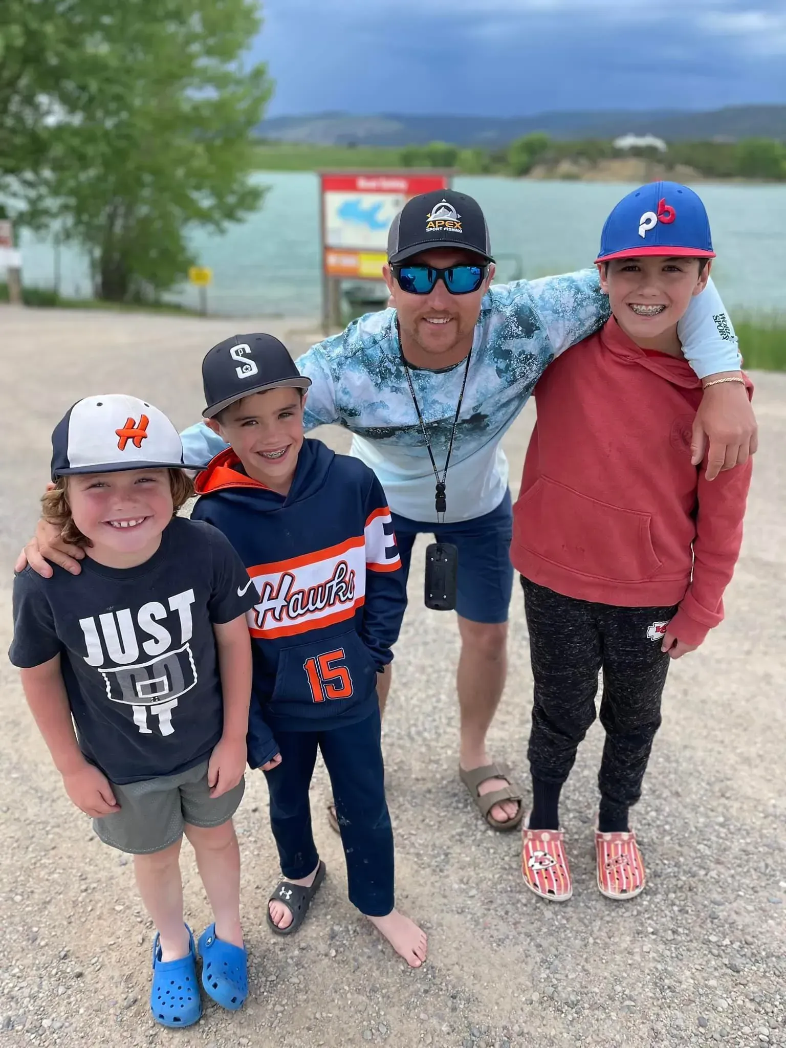 Man with three children standing near a lake, all wearing hats.