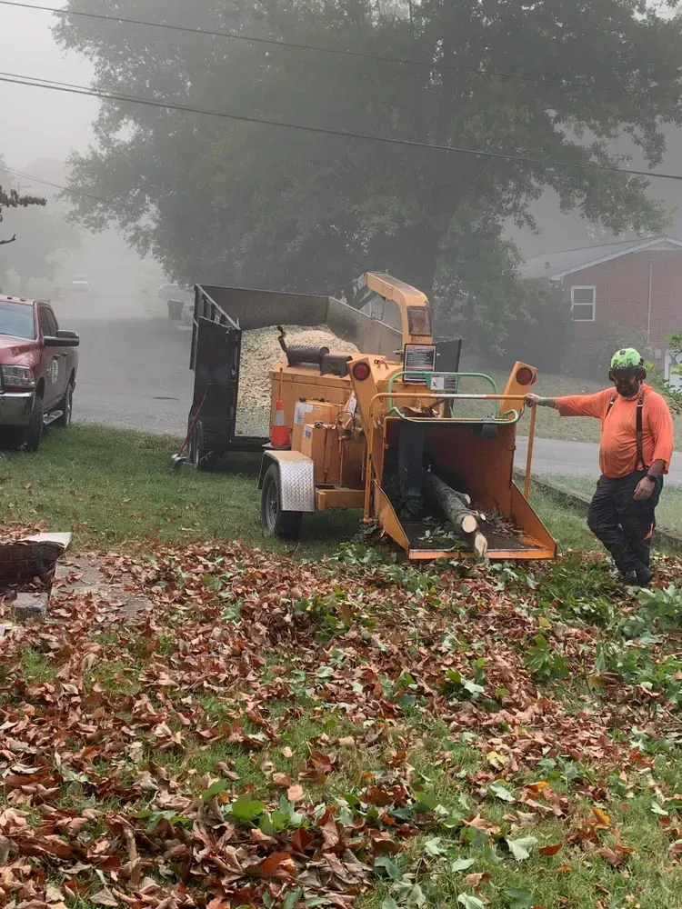 A man is standing next to a tree chipper in a yard.